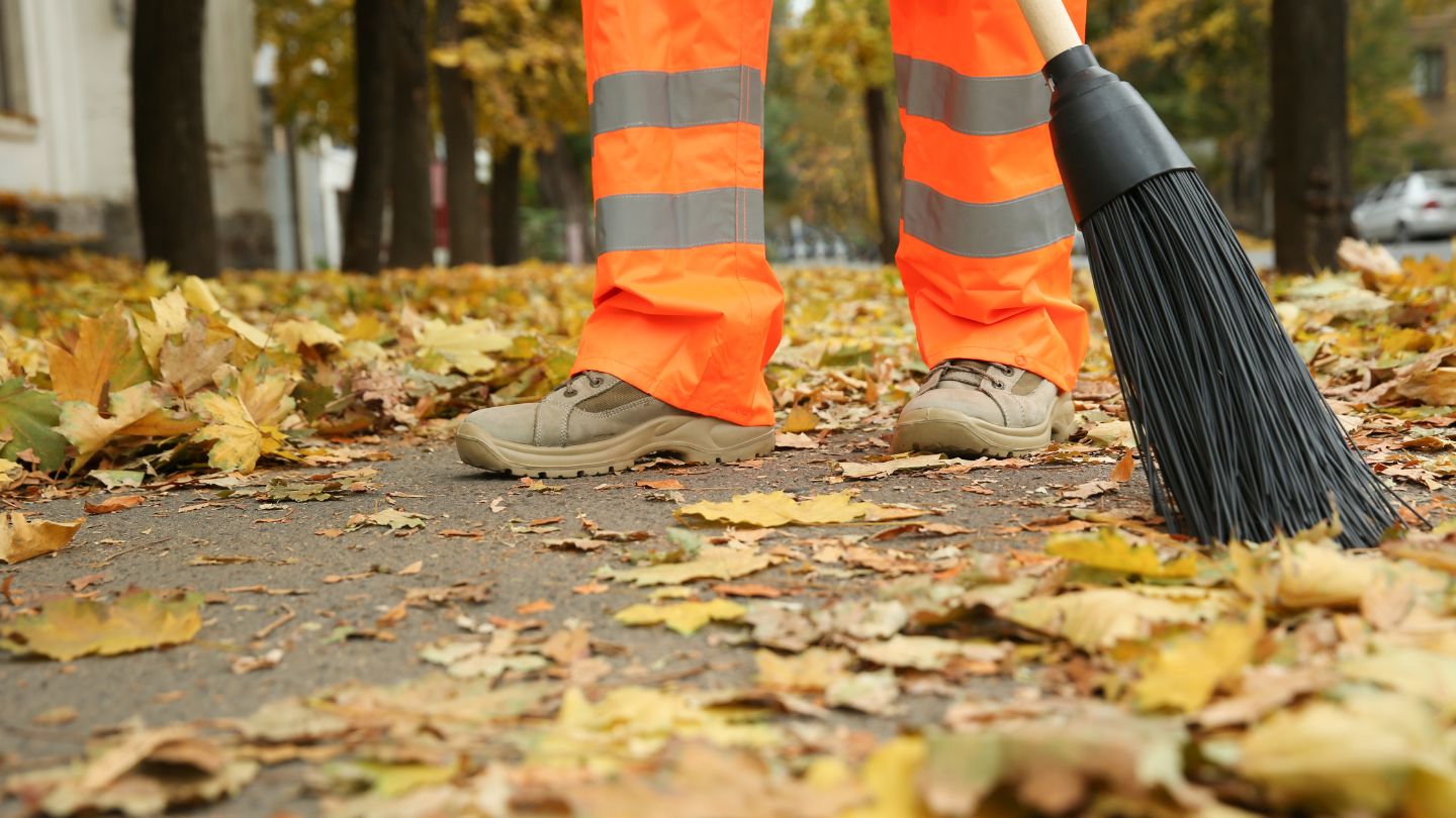 Worker sweeping autumn leaves on sidewalk.